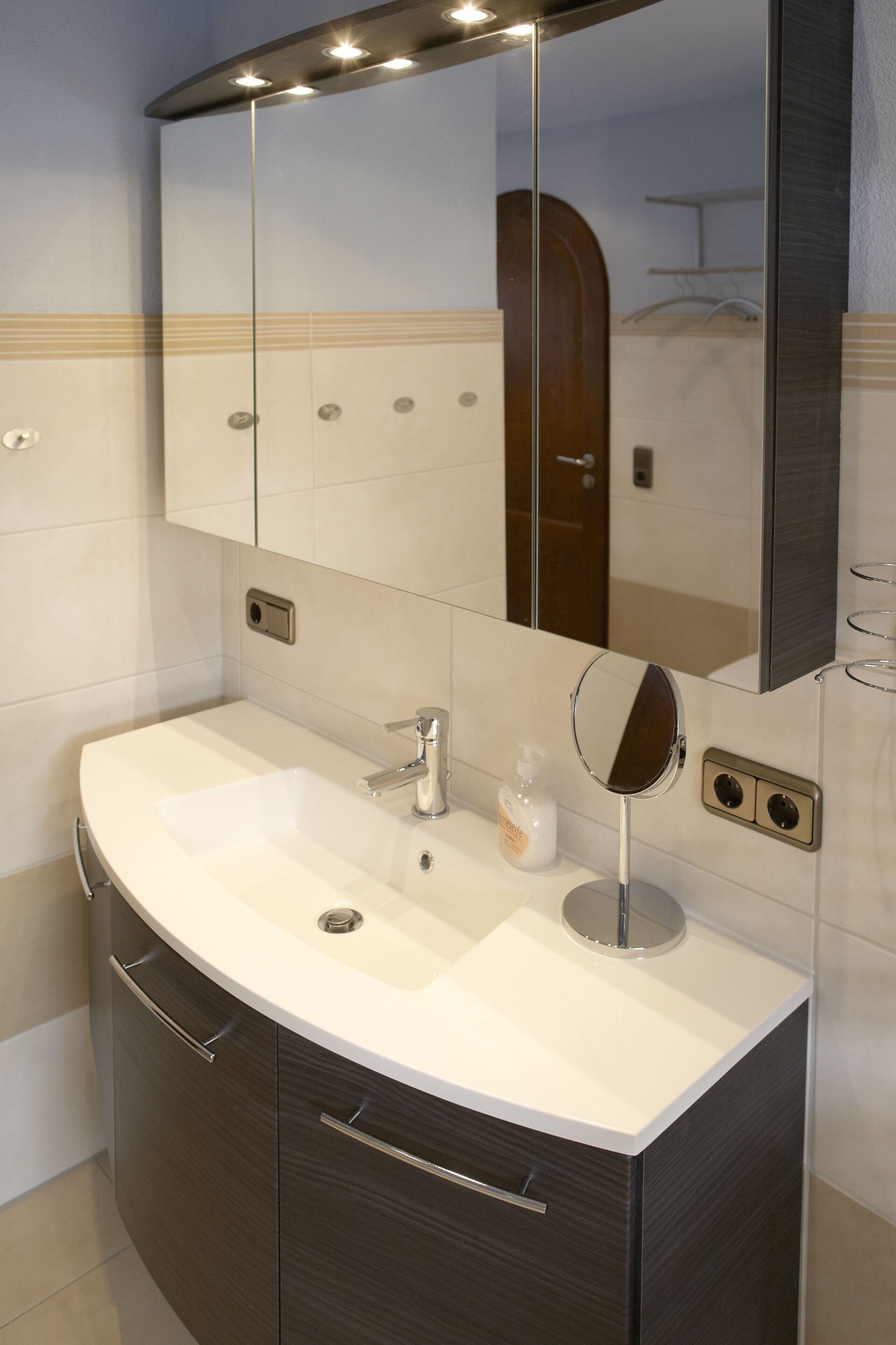 Un baño moderno con un tocador curvo, un espejo grande y un lavamanos integrado.