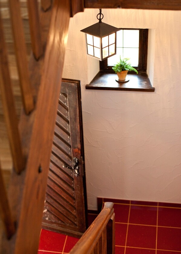 A wooden staircase with a lantern hanging above a window, a potted plant on the windowsill, and a red-tiled floor.