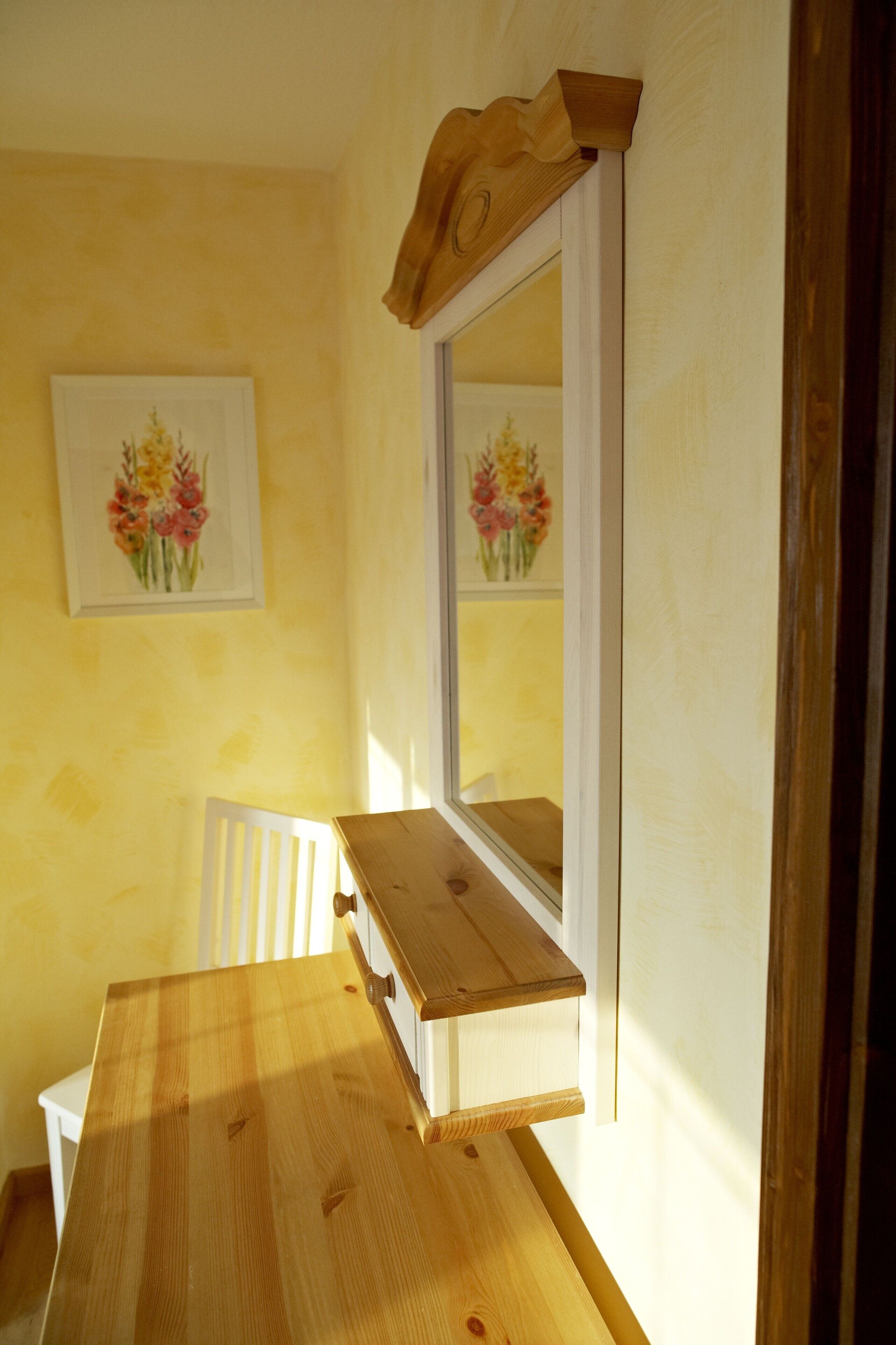 A room with a wooden table, a white chair, and a mirror on the wall.