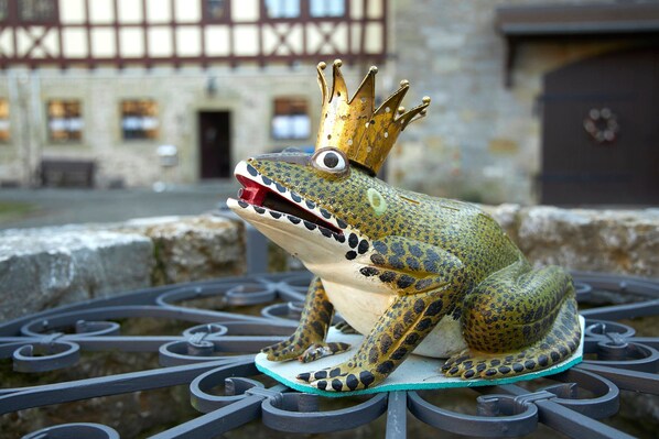 A frog statue with a crown on a metal bench.
