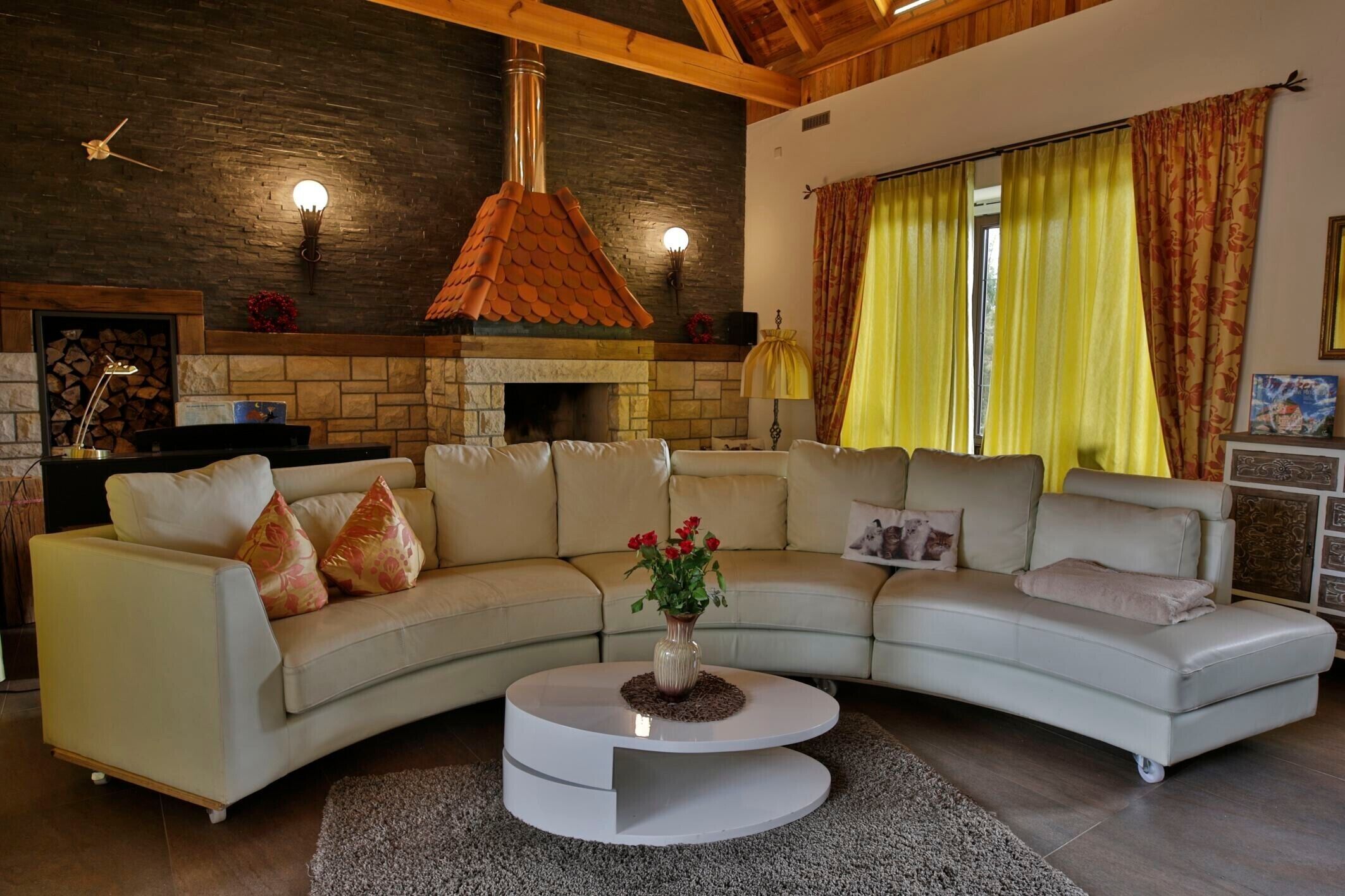 Uma sala de estar com lareira de pedra, um sofá branco e uma mesa de centro redonda.