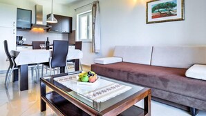 A modern living room with a brown sofa, a dining table with chairs, and a coffee table with fruit.