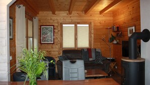 L’intérieur d’un chalet en bois comprend un canapé, une table à manger, une cheminée et une fenêtre avec des stores.