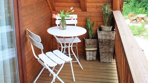 Un balcon en bois avec une table et des chaises, des plantes en pot et une vue sur la verdure.