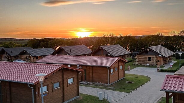 Une rangée de chalets en rondins, avec une allée pavée et un coucher de soleil en arrière-plan.