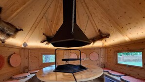 L’intérieur d’une cabane en bois, avec une table au centre, des bancs et une cheminée.