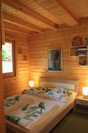 A wooden cabin room with a bed, bedside lamps, a framed picture, and a window.