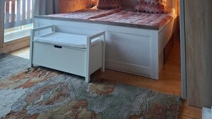 Une chambre avec un plafond en bois, un lit agrémenté de coussins à pois, une petite table de chevet blanche et une vue par la fenêtre.