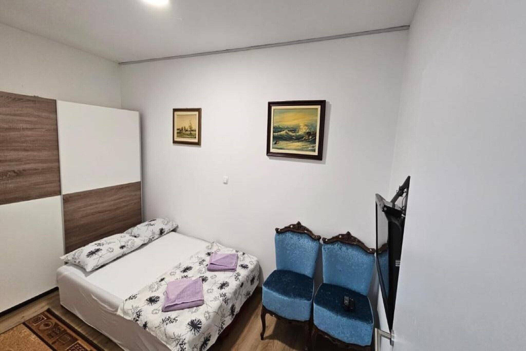 Une petite chambre à coucher, bien rangée, avec un lit, deux chaises et deux tableaux encadrés accrochés au mur.