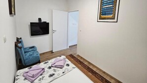 A small, tidy room with a bed, a chair, a television, and a door. - Apartment Gracac - Two Bedroom Apartment with Terrace (Gracac)