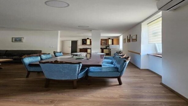 A spacious living area with a large wooden dining table surrounded by blue upholstered chairs, a dark-colored sofa, and a kitchen area in the background. - Apartment Gracac - Two Bedroom Apartment with Terrace (Gracac)