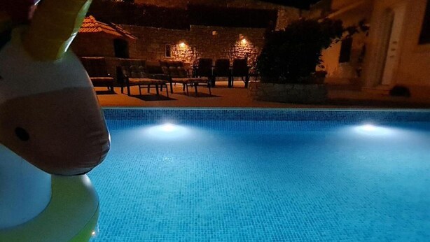 Une piscine dont le fond est recouvert de carrelage, entourée d’un espace de détente extérieur et de murs en pierre.