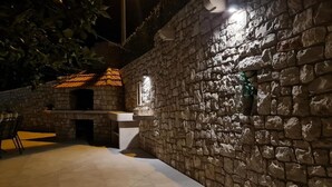 Un espace extérieur entouré de murs en pierre, doté d’un sol carrelé, d’un petit coin salon et d’un barbecue intégré.