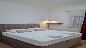Un lit bien fait, avec une tête de lit, une lampe de chevet et une fenêtre avec des rideaux.