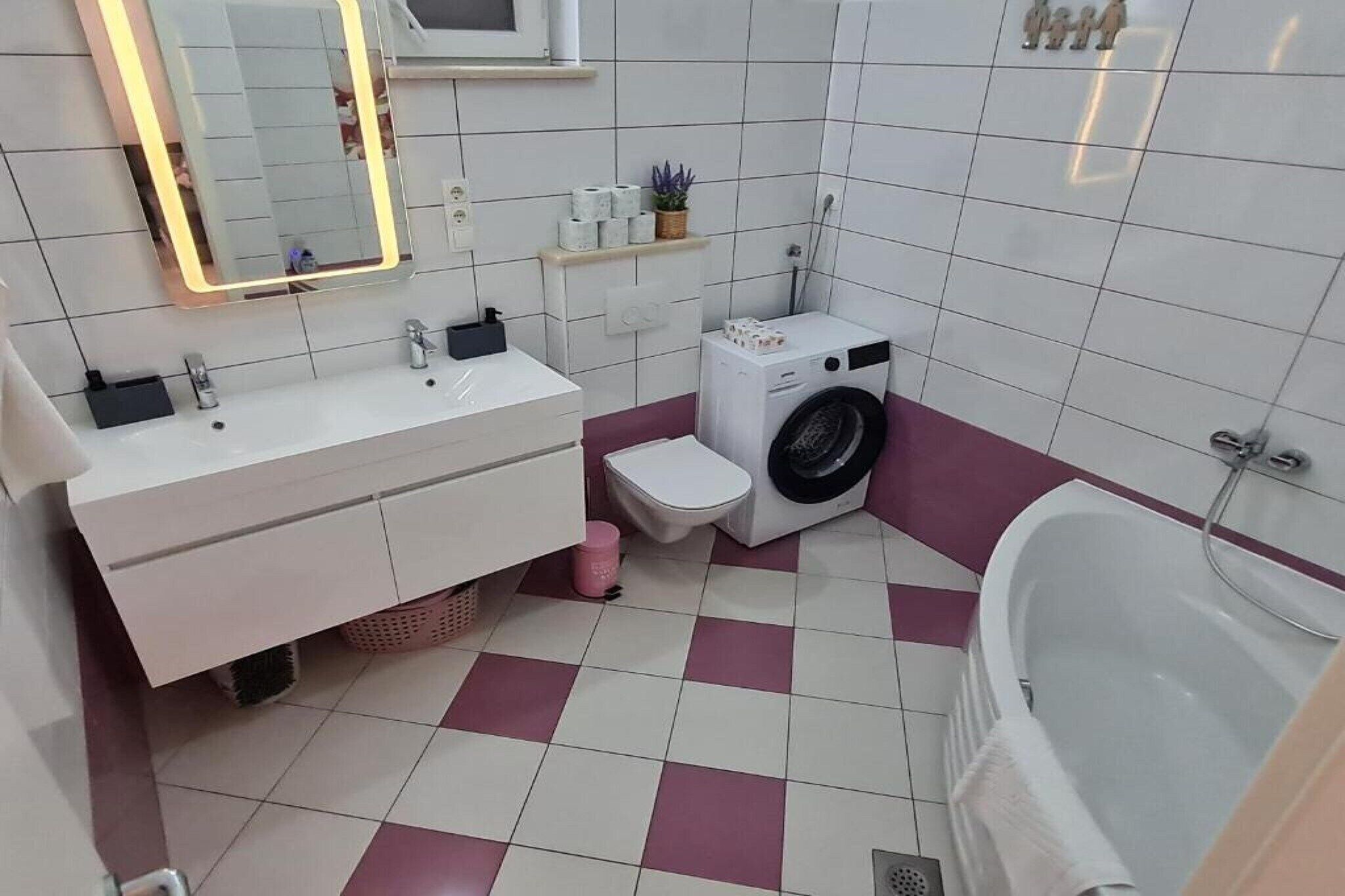 Un baño con lavamanos blanco, espejo, inodoro, lavadora y bañera.