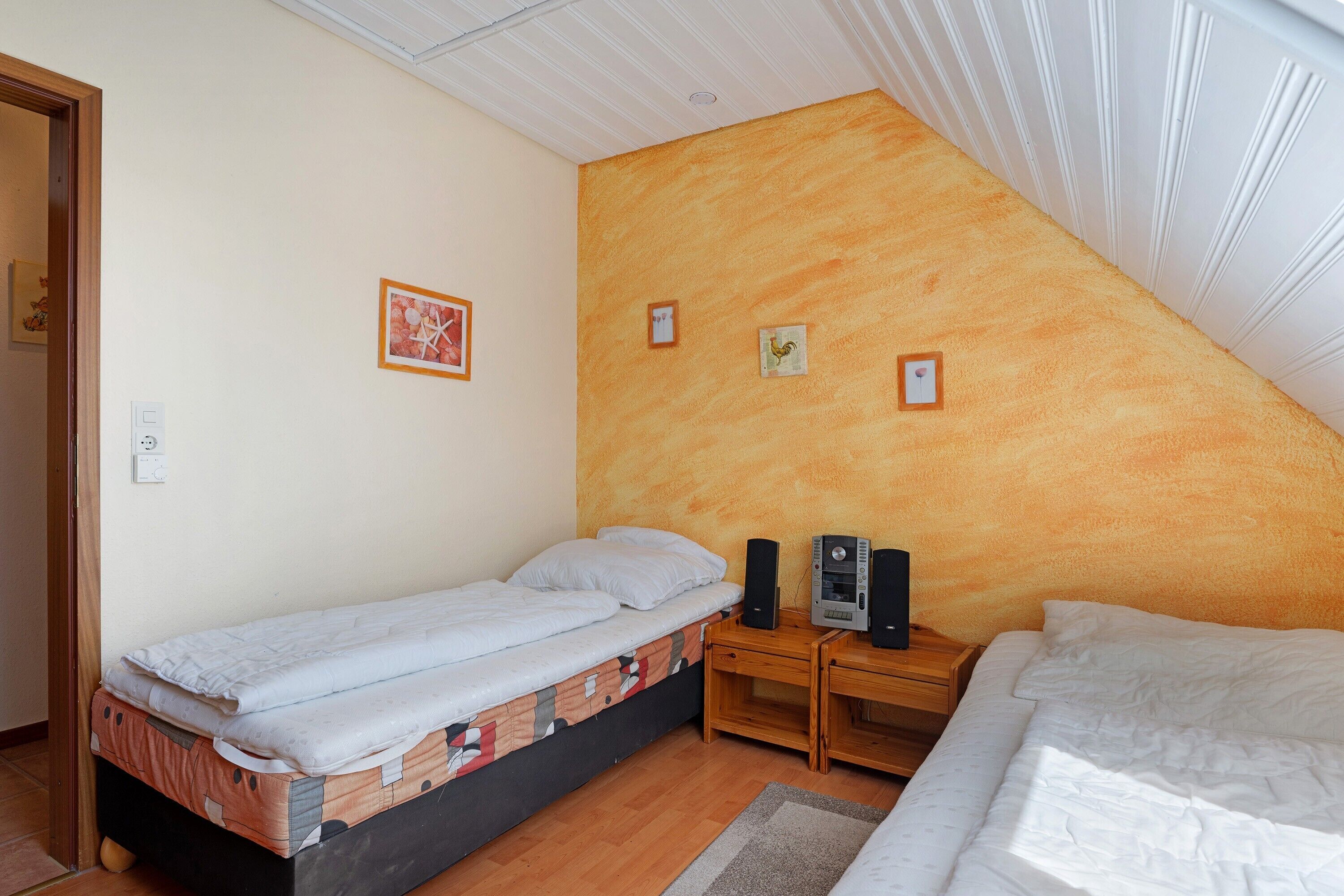Un dormitorio con cama, una mesita de noche de madera, un calentador de pared y una puerta.