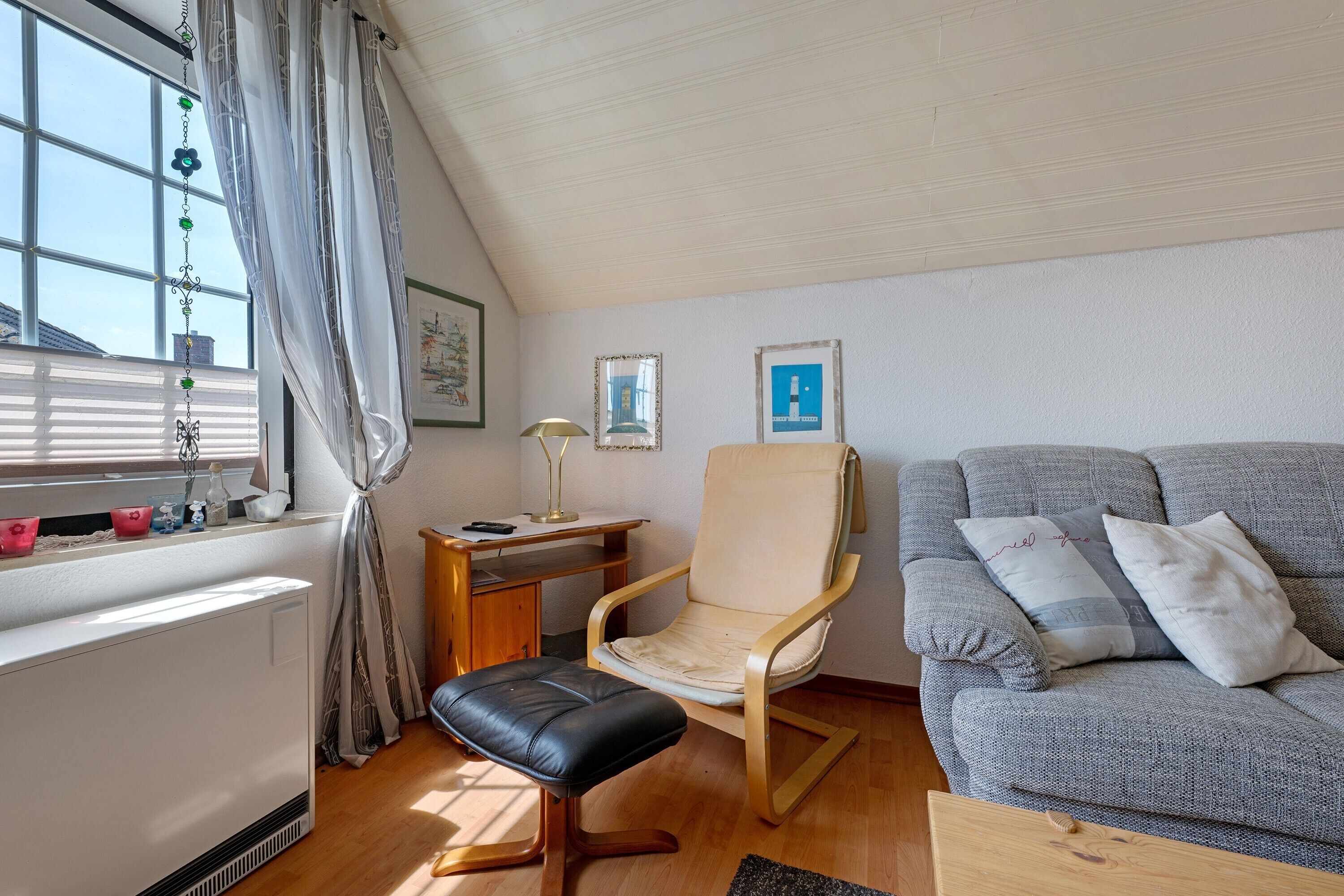 Una habitación con ventana, escritorio, silla, sofá y radiador.