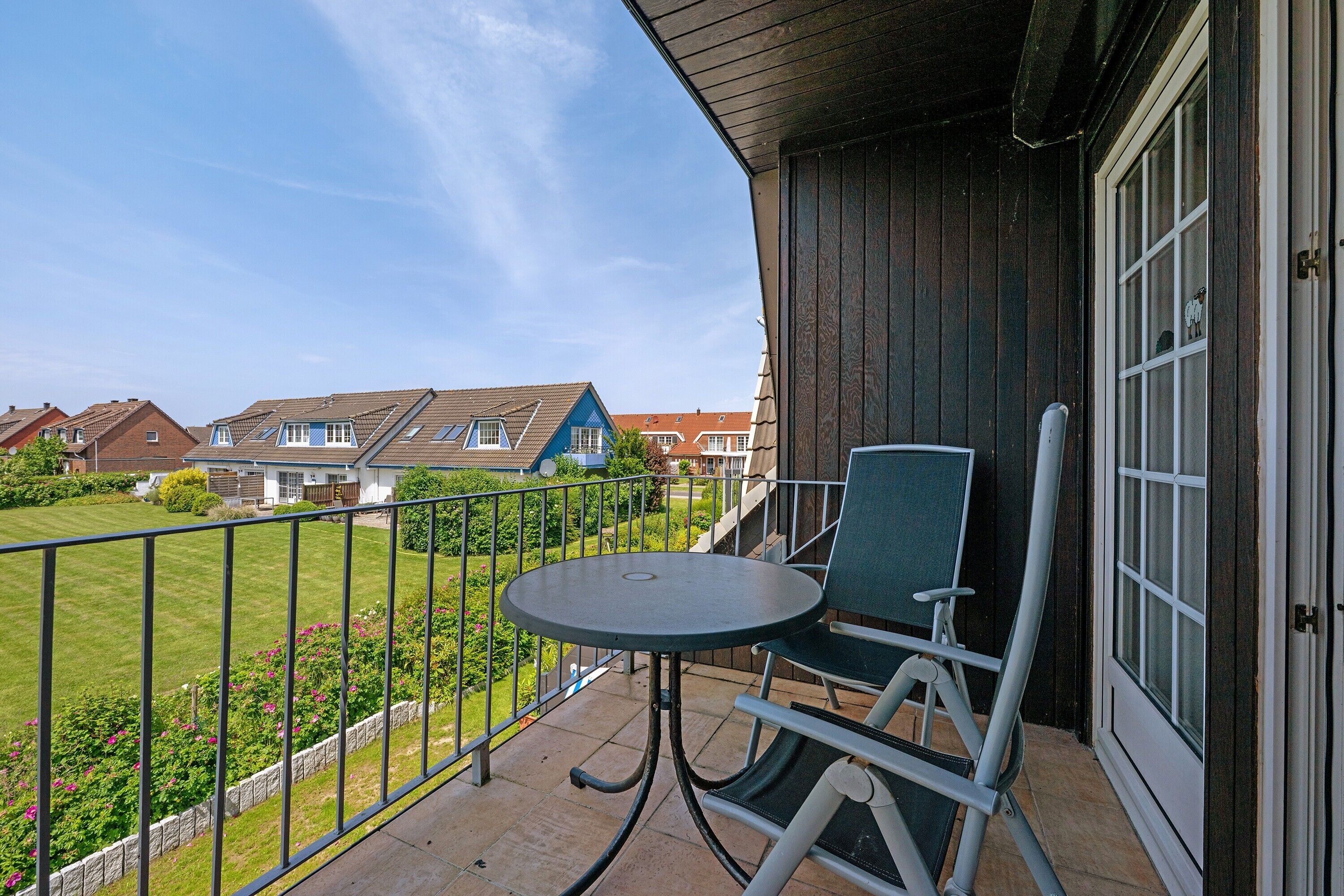 A balcony with a table and chairs, a view of neighboring houses, and a metal railing.