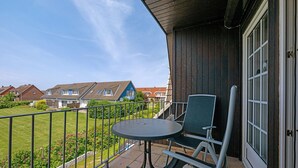 En balkon med et bord og stole, udsigt til nabohuse samt gelænder i metal.