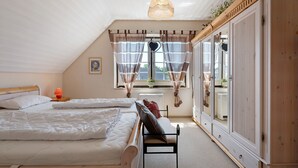 Et soveværelse med seng, bænk, spejl og et vindue med gardiner.
