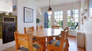 Spiseplads med et træbord og stole, en hængende lysekrone og udsigt til det fri gennem store vinduer.