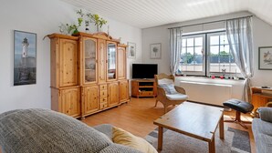 En stue med et træskab, et fjernsyn, et vindue med gardiner og en sofa.