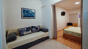 A room with a sofa, a bed, a TV, and a painting on the wall.