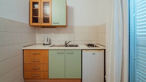 A compact kitchen with a sink, a kettle, and a refrigerator.