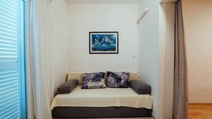 A small, cozy room with a bed, a painting on the wall, and a window with curtains.