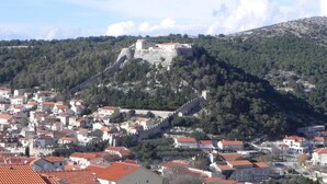 Un château fort historique, perché sur une colline et dominant une ville aux bâtiments aux toits rouges.