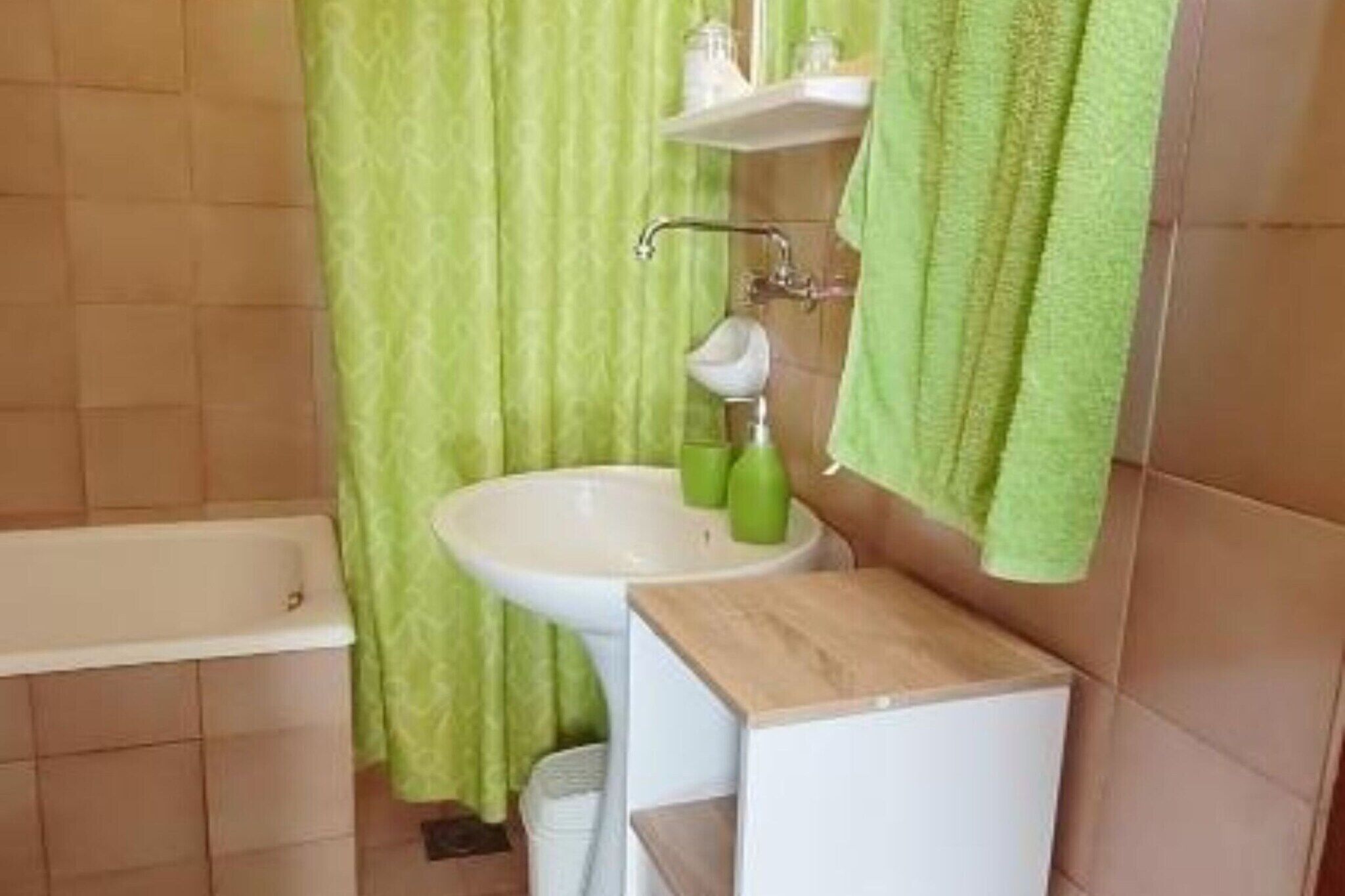 Une salle de bain avec une baignoire, un lavabo et des rideaux verts.