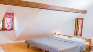A bedroom with a wooden bed, a sloped ceiling, and a window with a red checkered curtain.