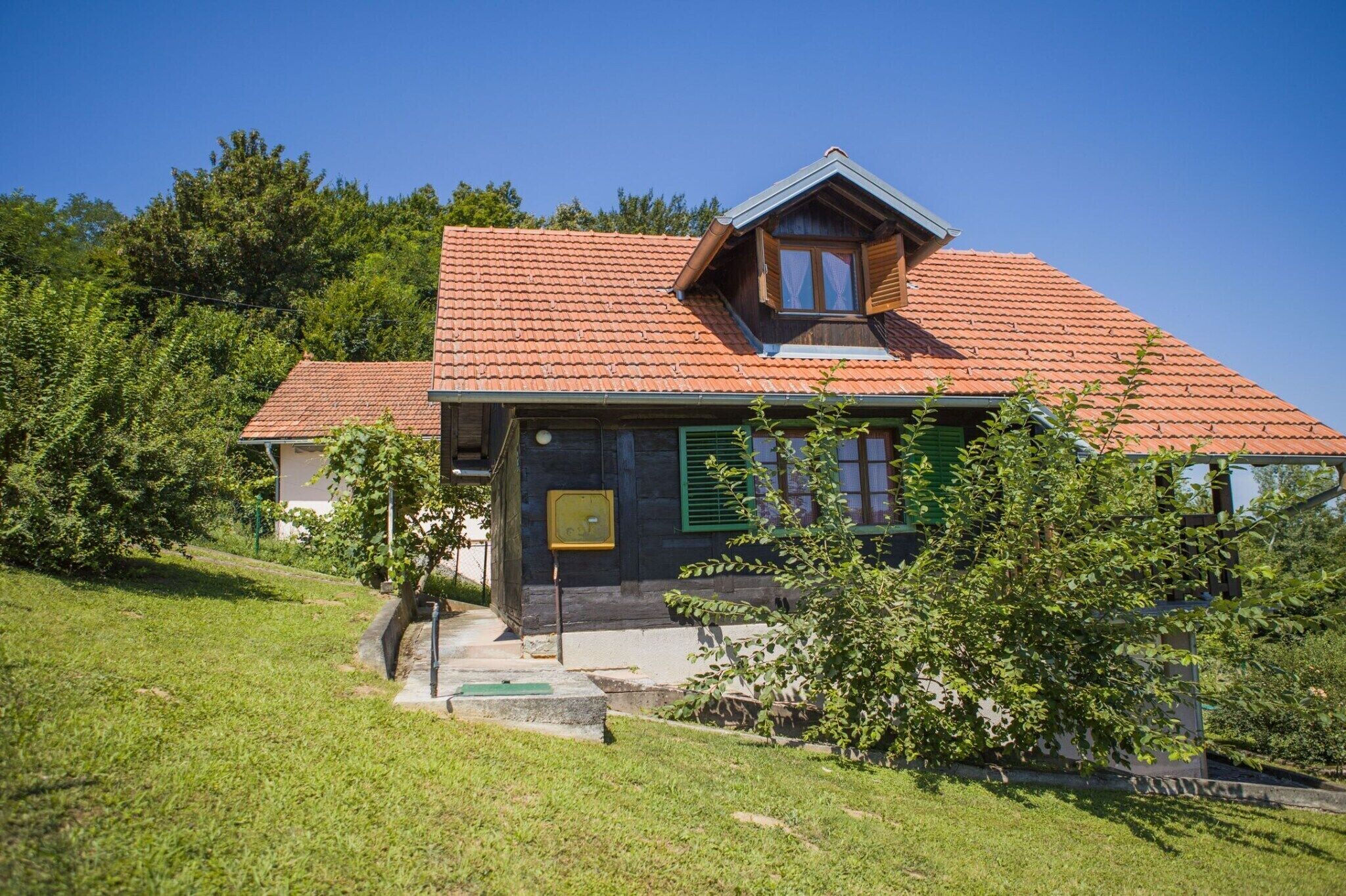 Een huis met één verdieping, een rode dakbedekking van tegels, groene luiken en een klein terras.
