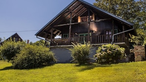 A wooden cabin with a balcony, surrounded by greenery.