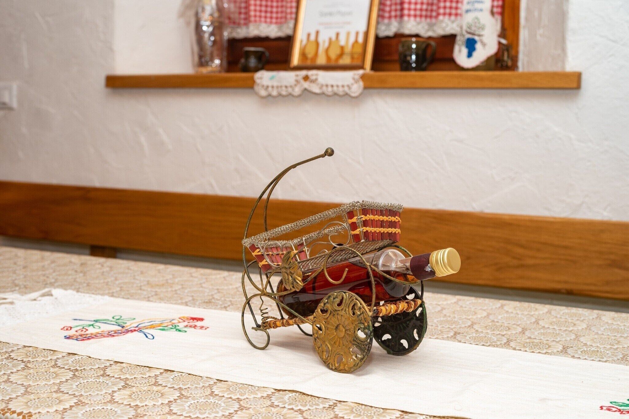 Un pequeño carruaje ornamentado con una botella de vino sobre un mantel de encaje.