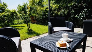 Ein Sitzbereich im Freien mit Korbmöbeln und einem Tisch mit Kuchen und Tasse.