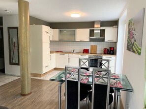 A modern kitchen with white cabinets, a glass dining table, and a coffee machine.
