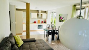Ein modernes Wohnzimmer mit Sofa, Esstisch und einer Küche im Hintergrund.
