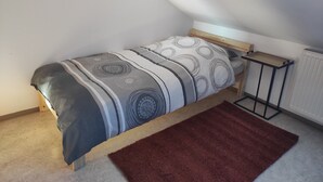 A single bed with a patterned bedspread, a wooden headboard, a small bedside table, and a radiator.