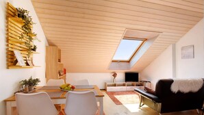 A modern loft apartment with a dining area, a sofa, a TV, and a skylight.