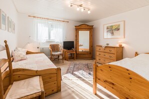 Quarto com duas camas de madeira, cômoda de madeira, televisão, cadeira e espelho.