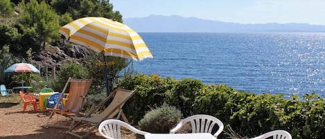 Uma área de estar à beira-mar com mesa e cadeiras, um guarda-sol listrado e vista para o mar.