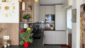 A modern kitchen with white cabinets, a wooden shelf with decorative items, and a clock on the wall.