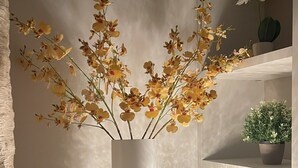 A modern interior with a round table, a white vase with yellow flowers, a textured globe lamp, and a potted plant on a shelf.