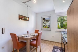 Un comedor con una mesa y sillas de madera, un cuadro en la pared y un ventanal con vistas a zonas verdes.