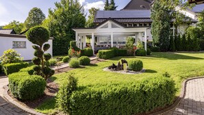 Uma casa moderna com varanda coberta, rodeada por jardins bem cuidados e telhado com painéis solares.