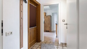 Um corredor com porta de madeira, um interruptor de luz e chão de azulejos.