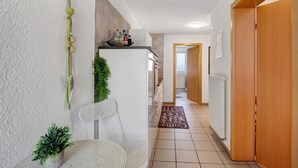 Un pasillo con una silla blanca, una mesita, un refrigerador y un radiador.