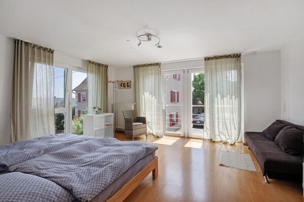 A bedroom with a bed, a sofa, a chair, and a window with curtains.