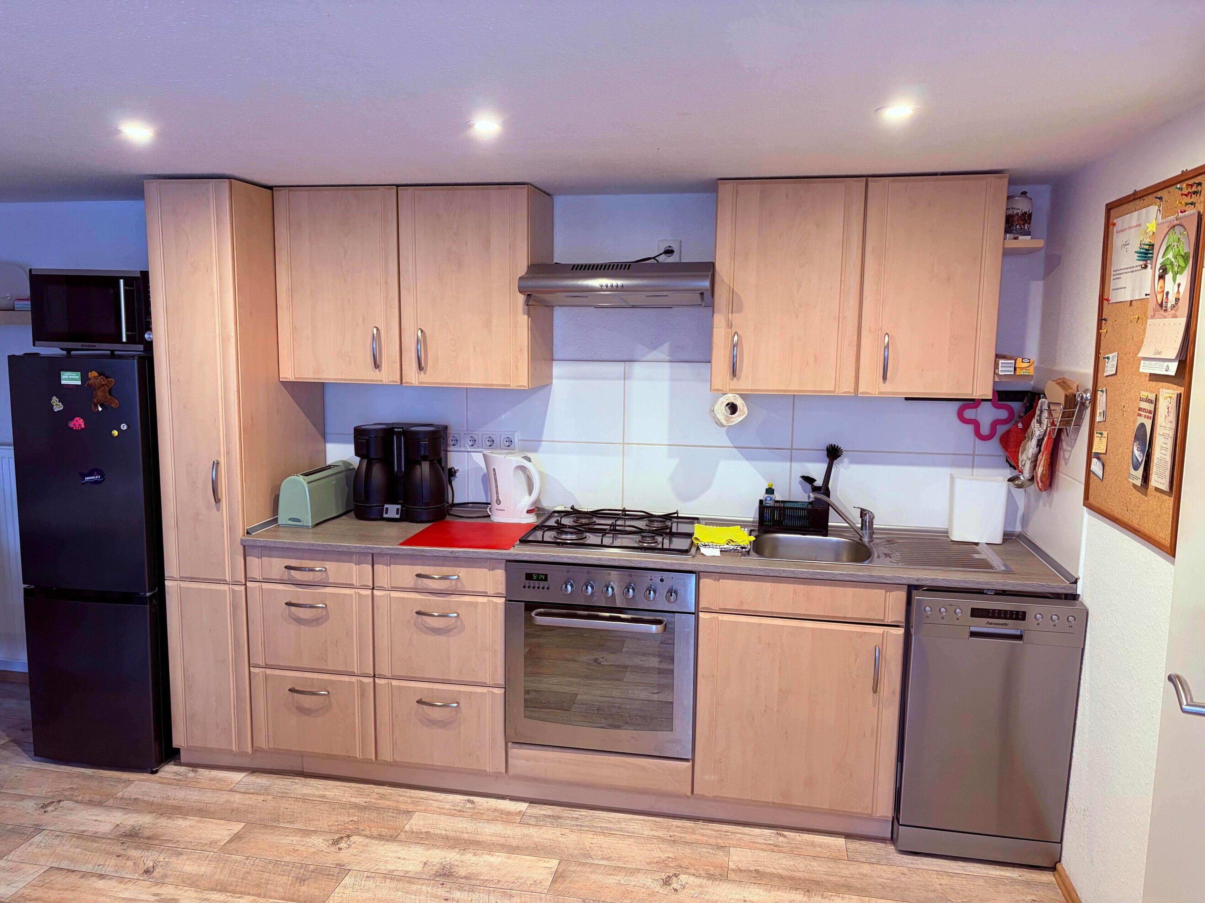 A modern kitchen with wooden cabinets, a black refrigerator, a stove, and a dishwasher.